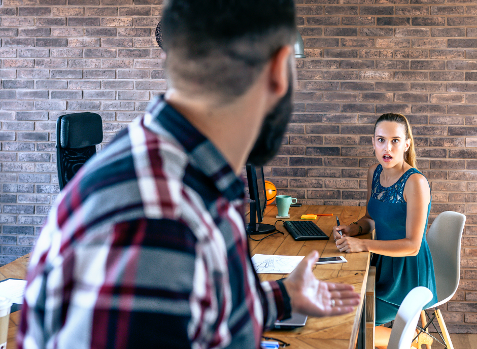 Woman sitting at a desk working, looking shocked at a man.